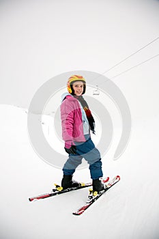 Young active girl skies downhill without sticks in yellow helmet and pink coat. Cut out, separated by snow and fogy weater.
