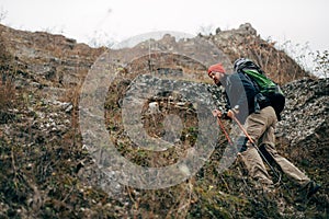 Young active male hiking in mountains with travel backpack. Traveler bearded man trekking and mountaineering during his journey