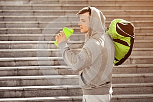 Young active man drinking water, outdoors. Handsome muscular male holding shaker