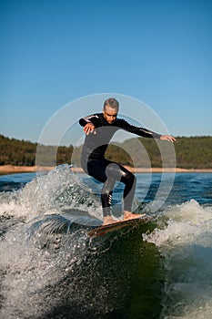 young active man energetically balancing on a wave on a wakesurf board