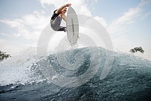 Young active man jumping up on the white wakeboard on the high b