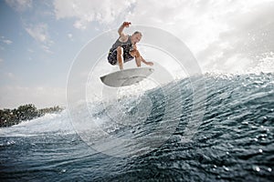 Young active man jumping on the white wakeboard down the blue wa