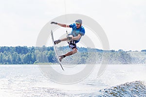 Young active man riding wakeboard on a wave from a motorboat on summer lake