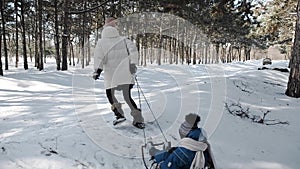 Young active mother pulls a sleigh with her child in a winter park