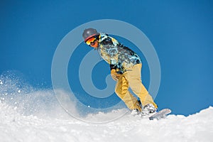 Young active snowboarder in bright sportswear riding down a mountain slope
