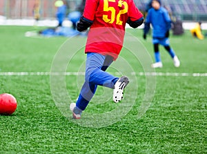 Young Active sport heathy boy in red and blue sportswear running and kicking a red ball on football field