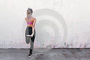 young active sport woman stretching quads on a wall. Home backyard workout. Copy space.