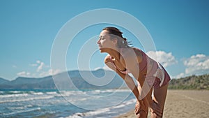 young active sporty athlete smiling woman is taking a break after making running and jogging workout on sea sandy beach