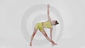 Young active sporty woman wearing yellow sportsuit doing Trikonasana pose, practicing yoga, full length shot