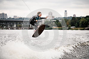 Young active woman rides wakeboard and jumps holds her hands on rope