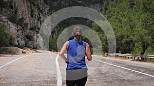 Young active woman running on mountain road. Energetic motivated fitness female jogging outdoors at sunny summer day. Athletic wom