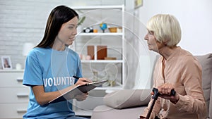 Young activist making list listening to aged lady walking stick, nursing home