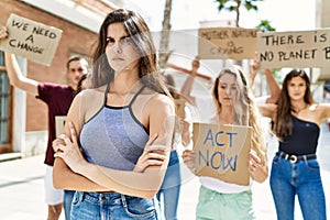 Young activist woman with arms crossed gesture standing with a group of protesters holding banner protesting at the city
