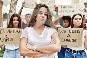 Young activist woman with arms crossed gesture standing with a group of protesters holding protest banner at the city