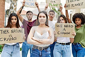 Young activist woman with arms crossed gesture standing with a group of protesters holding protest banner at the city