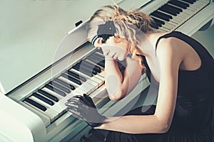 Young actress lying on piano overwhelmed with memories. Sad blond girl leaning on keyboard. Roaring twenties fashion