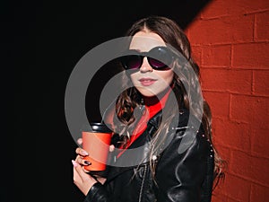 Young adorable brown haired teen model in sunglasses trendy makeup adorable smile red dress black leather jacket holding red