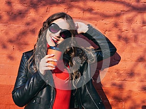 Young adorable brown haired teen model in sunglasses trendy makeup adorable smile red dress black leather jacket holding red