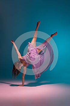 Young adorable flexible contemp dancer in lilac dress dancing  on gradient blue white background in neon.