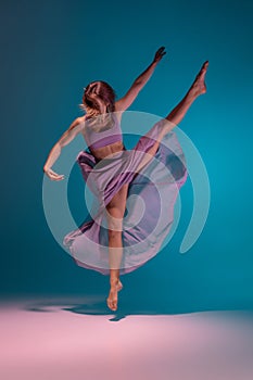 Young adorable flexible contemp dancer in lilac dress dancing isolated on gradient blue white background in neon.