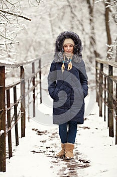 Young adorable woman wearing blue hooded coat enjoying strolling in winter forest outdoors. Nature cold season freshness concept.