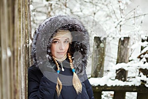 Young adorable woman wearing blue hooded coat enjoying strolling in winter forest outdoors. Nature cold season freshness concept.