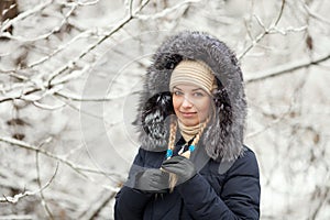 Young adorable woman wearing blue hooded coat enjoying strolling in winter forest outdoors. Nature cold season freshness concept.