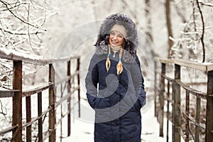 Young adorable woman wearing blue hooded coat enjoying strolling in winter forest outdoors. Nature cold season freshness concept.