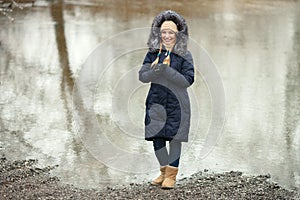 Young adorable woman wearing blue hooded coat enjoying strolling in winter forest outdoors. Nature cold season freshness concept.