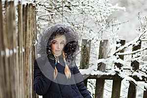 Young adorable woman wearing blue hooded coat enjoying strolling in winter forest outdoors. Nature cold season freshness concept.