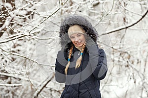 Young adorable woman wearing blue hooded coat enjoying strolling in winter forest outdoors. Nature cold season freshness concept.