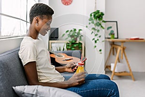 Young adult african woman using mobile phone while relaxing on sofa at home