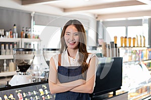 Young adult Asian business woman crossing her arms in front of cafe restaurant while smiling. Happy barista of Coffee