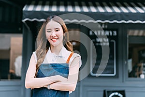 Young adult Asian business woman crossing her arms in front of cafe restaurant while smiling. Happy barista of Coffee