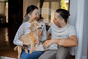 Young adult Asian couple holding a puppy with home interior in background. 30s mature woman holding a dog pet talking