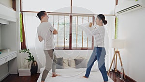 Young adult Asian couple playing pillow fight in bedroom interior scene. 30s mature husband and wife smiling and having