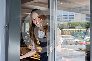 Young adult Asian female barista welcoming a customer walking into the coffee shop with a friendly smile and warm