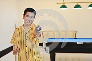 Young adult asian man showing number 8 black billiard or snooker ball with confident and happy smiling face after finish game in