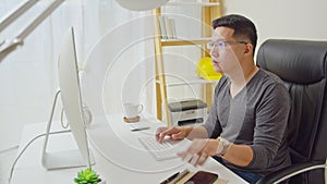 Young adult Asian man work at home or modern office, using desktop computer and smartphone. Work from home life concept