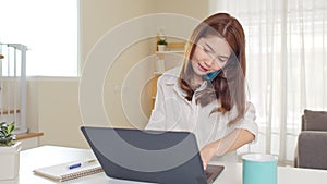 Young adult asian woman work at home or modern office, using laptop computer and smartphone. Work from home life concept