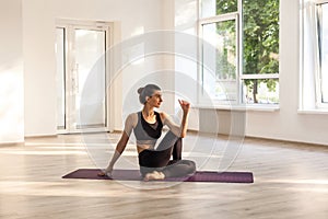 Young adult attractive smiling woman practicing yoga, sitting in ardha matsyendrasana exercise, half lord of fishes pose, working