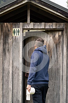 Young adult backpacker entering to rustic wooden toilet in outdoors background