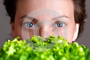 Young adult beautiful caucasian happy smiling woman portrait holding green fresh lettuce salad crop in front face