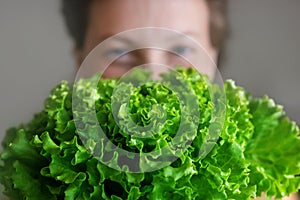 Young adult beautiful caucasian happy smiling woman portrait holding green fresh lettuce salad crop in front face. Healthy food