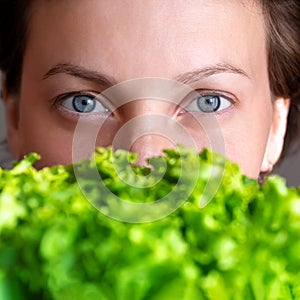 Young adult beautiful caucasian happy smiling woman portrait holding green fresh lettuce salad crop in front face. Healthy food