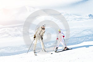 Young adult beautiful sporty mother having fun skiing with kid daughter on mountain alpine ski winter resort. Slim mom