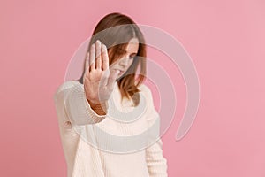 Young adult blond woman standing with stop gesture, looking away, caution to dont touch.