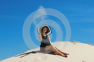 Young adult brunette woman relaxing on a beach. Happy Woman playing with sand at the beach. Pretty woman throwing sand up.