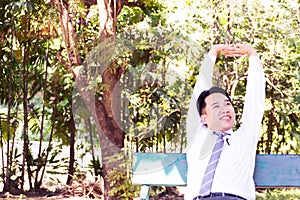 Young adult businessman sitting and relaxing in park. Stretching