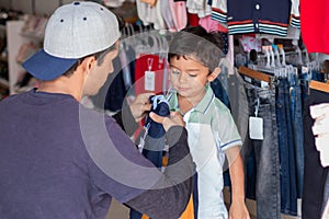 Young adult buying clothes for his son, latin man sizing a shirt or sweater for his son in a clothing store.
